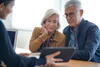 an older woman and man look at a tablet being shown to them by a woman